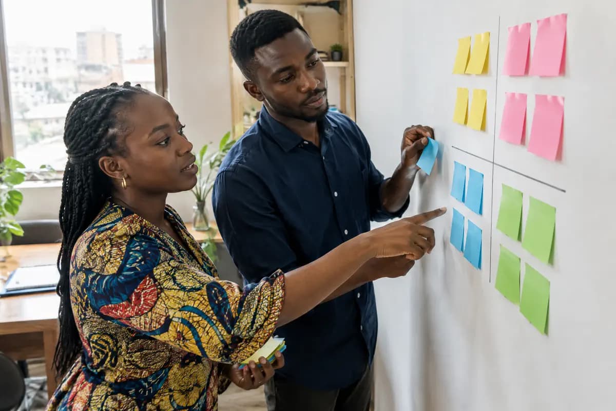 Deux collègues répartissent des notes adhésives de couleur en quatre zones sur un mur de bureau.